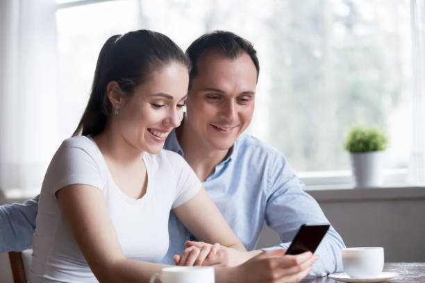 istock Smiling couple reading funny message on phone at home 1155911466