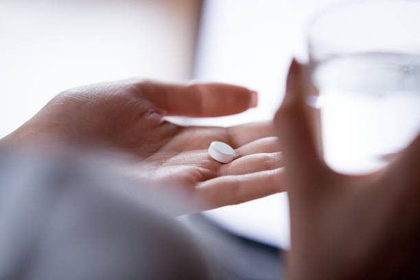 donna da vicino che tiene la pillola in mano con l'acqua - painkiller pill capsule birth control pill foto e immagini stock