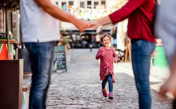 istock A small girl running towards unrecognizable parents outdoors in town. 1155912108
