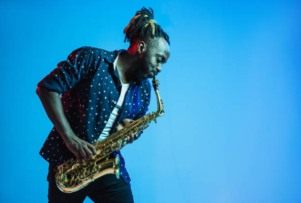 Young african-american jazz musician playing the saxophone Young african-american jazz musician playing the saxophone on blue studio background in trendy neon light. Concept of music, hobby. Joyful attractive guy improvising. Retro colorful portrait of artist. sax arts and crafts stock pictures, royalty-free photos & images
