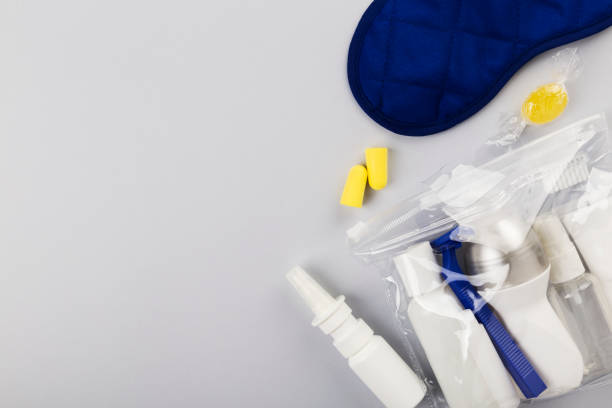 istock Set for flight small bottles with cosmetics, sleep mask, earplugs, nasal spray on gray background. Top view, copy space 1155918813
