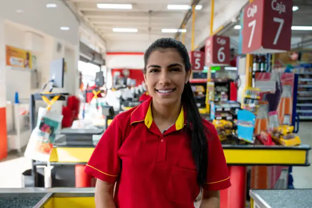 Portrait of a happy cashier working at the supermarket and looking at the camera smiling - business concepts