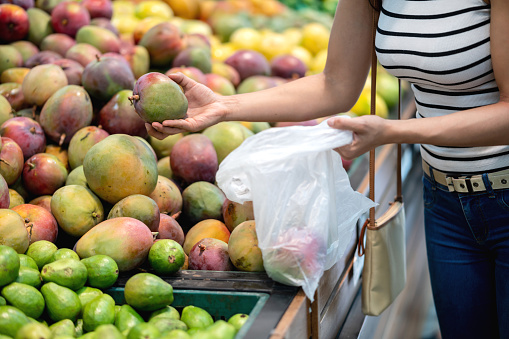 Close-up on a woman shopping for fruits at the supermarket and picking up some mangoes - lifestyle concepts