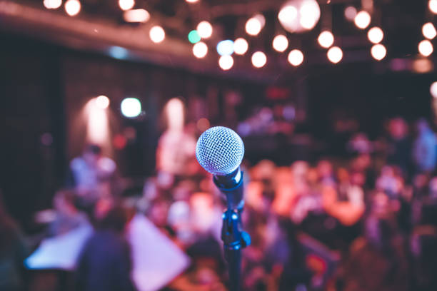 Event hall: Close up of microphone stand, seats with audience in the blurry background stock photo
