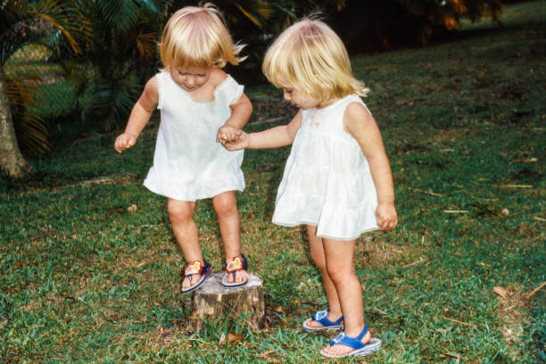 Color image of happy twin, blonde-haired girls sitting together outside on a summer day.