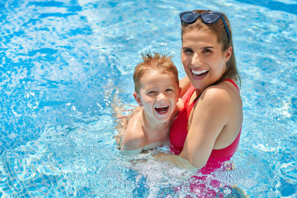 ragazzo carino con sua madre che gioca in piscina durante l'estate - mother enjoyment built structure human head foto e immagini stock