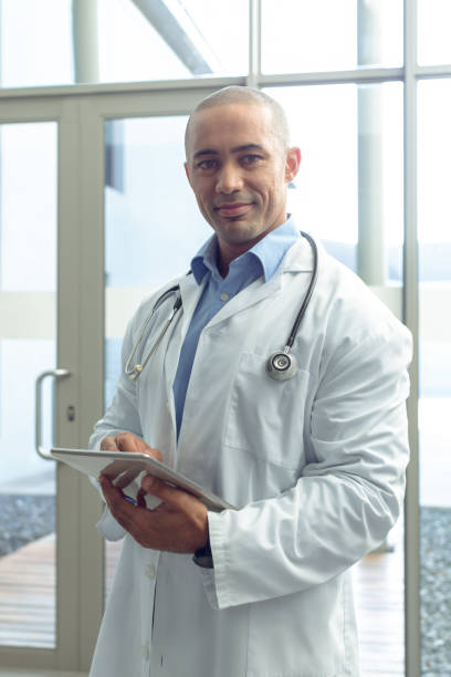 istock Male doctor looking at camera while using digital tablet in lobby at hospital 1155930110