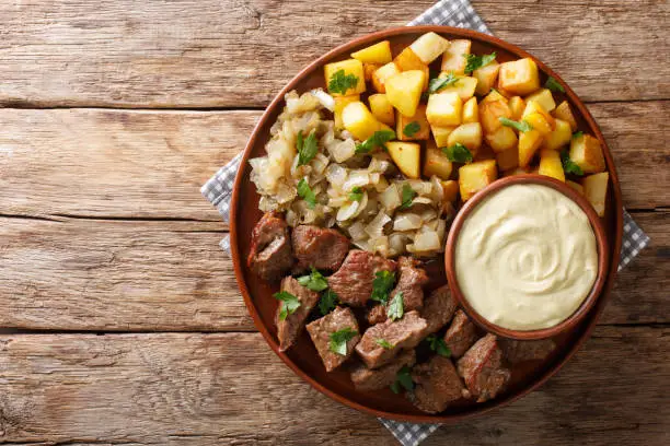 Swedish Beef Rydberg with fried onions and crisp potatoes with mustard sauce close-up on a plate on the table. Horizontal top view from above