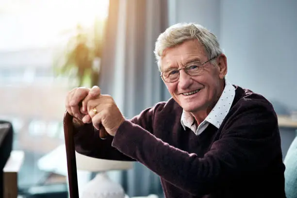 Portrait of a senior man sitting at home with a walking stick