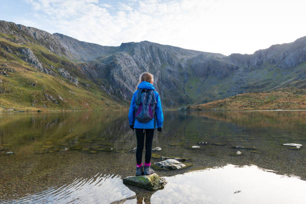 Girl looking out over mountain lake Girl standing on rock looking out over mountain lake. snowdonia national park stock pictures, royalty-free photos & images