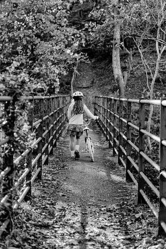 Girl pushing bike over bridge in black and white