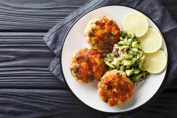 Photo of Delicious healthy salmon fritters with avocado salsa and lime closeup on a plate. horizontal top view