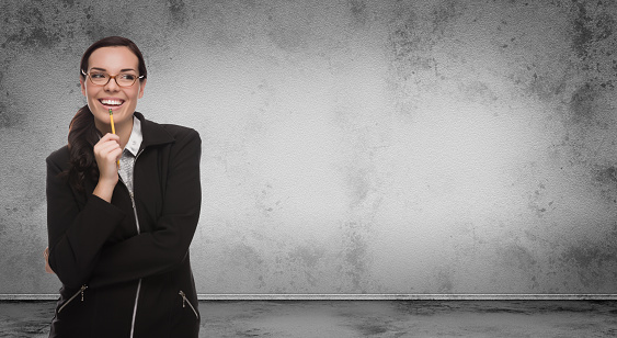 Young Adult Woman with Pencil and Glasses Standing In Front of Blank Grungy Blank Wall with Copy Space.