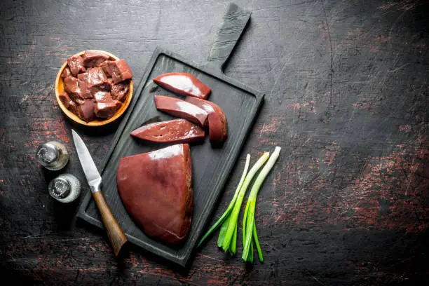 Pieces of raw liver in a plate and on a cutting Board. On dark rustic background