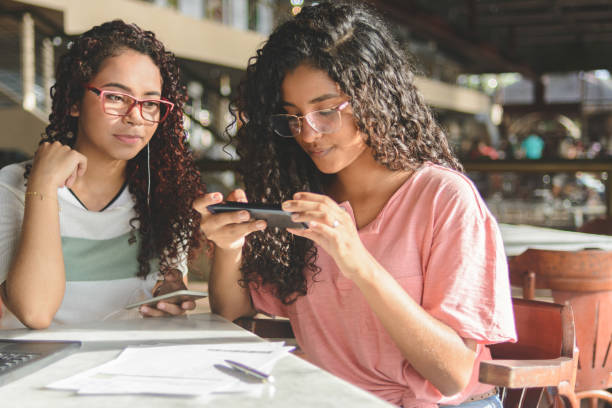 オンラインバンキングアプリを介して紙幣の支払いのためのバーコードのスマートフォンで写真を撮る2人の若い女性 - ラテンアメリカ 写真 ストックフォトと画像