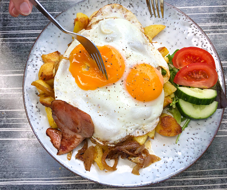 Dutch Cuisine: Soft Fried Eggs Atop Hashed Browns and Ham. Two forks digging in. Shot in Friesland, Holland.