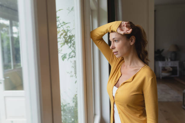 istock Beautiful woman with arm on forehead looking outside through window in a comfortable home 1155957177