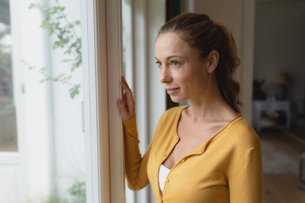 istock Woman looking outside through window in a comfortable home 1155957201