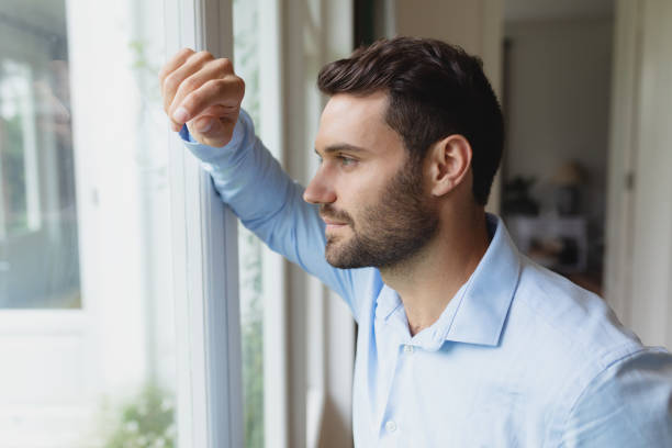 istock Thoughtful man looking outside through window in a comfortable home 1155958011