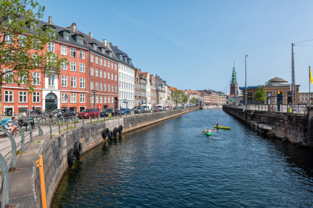 Canal, Nybrogade, Christiansborg, Copenhagen. City street with two kayaks on waterway and people in the background.