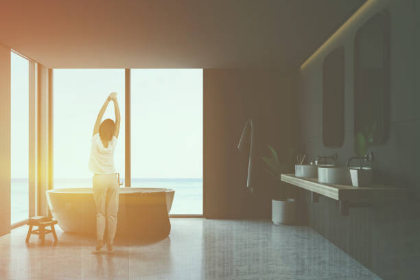 istock Woman in gray tile bathroom interior tub and sinks 1155958294