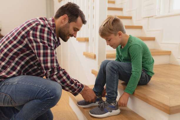 Father tying his sons shoelaces in a comfortable home Side view of Caucasian father tying his sons shoelaces in a comfortable home child tied up stock pictures, royalty-free photos & images