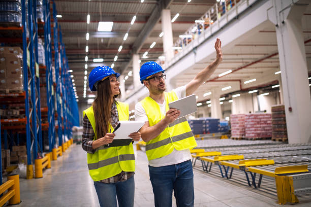 istock Warehouse workers consulting each other in large factory storage area. 1155959656