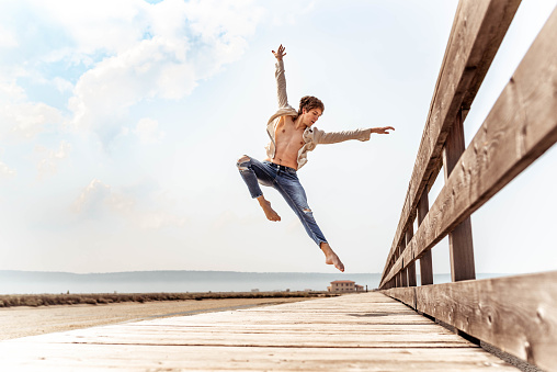 Young caucasian dancer jumping on a wooden pier.