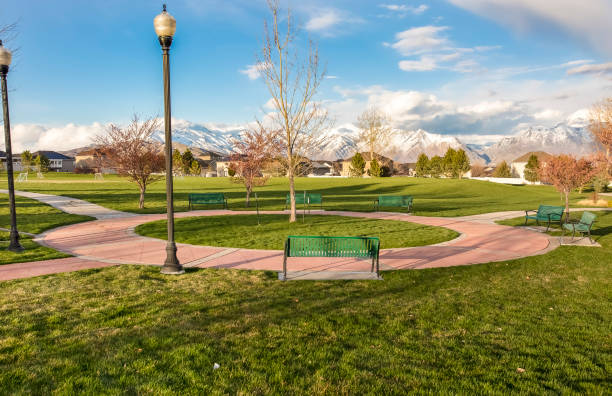 Green benches around a circular pathway on a park with trees and lamp posts