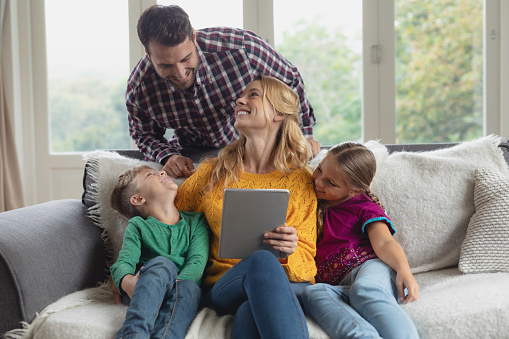Front view of happy Caucasian family using digital tablet on the sofa in a comfortable home