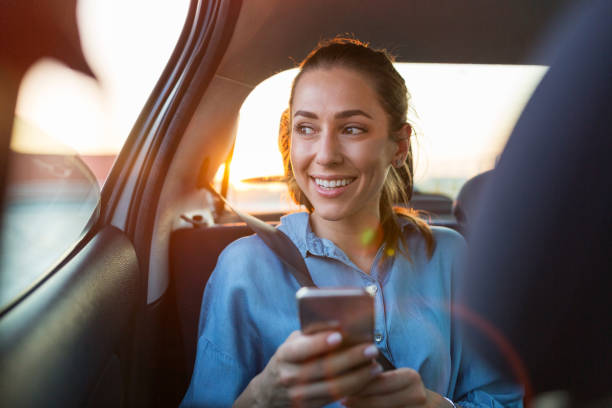 mujer joven con teléfono inteligente en el asiento trasero de un coche - taxi fotografías e imágenes de stock