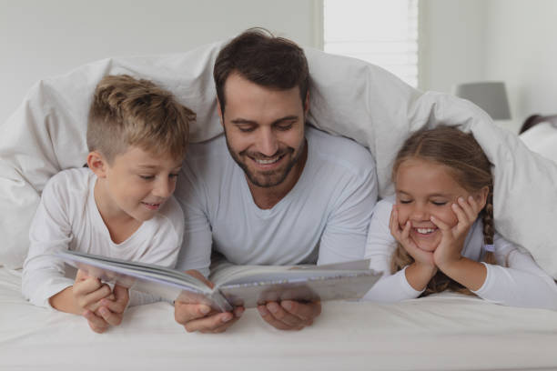 Father and children reading a book under blanket