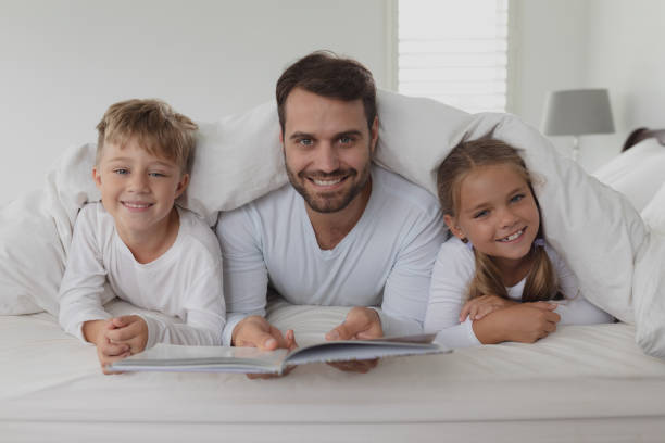 istock Father and children reading a book under blanket 1155966075