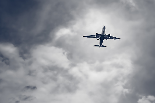 Passenger airplane flying on storm dark clouds background. Plane landing silhouette, bottom view.