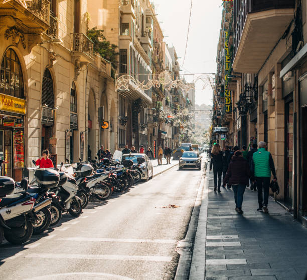 Barcelona, Spain - Nov 14, 2017: Typical day over Carrer Nou de la Rambla street with pedestrians tourists parked cars and motorcycles on a warm autumn day with beautiful warm sunlight flare