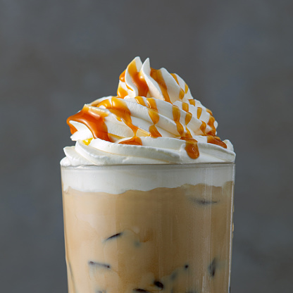 iced coffee latte decorated with whipped cream and caramel sauce on gray background