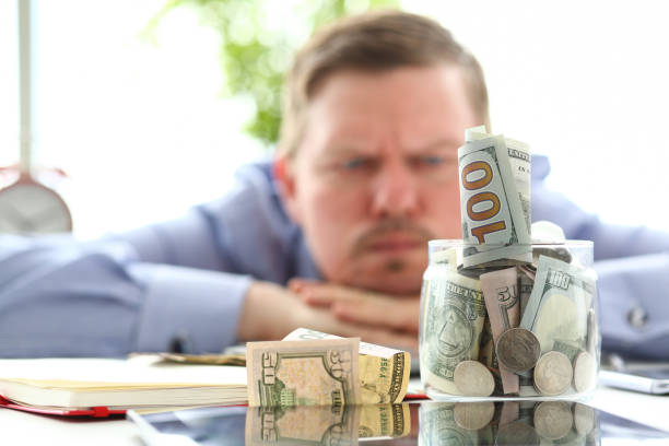 istock Man looking at jar full of money thinking about his debts 1155986697