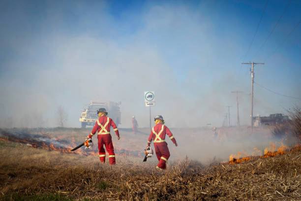firemen fighting a fire in a ditch beside highway horizontal image of a group of firemen fighting a fire burning in a ditch beside the highway  with smoke filling the air with the firetruck sitting by on a summer day. ditch stock pictures, royalty-free photos & images