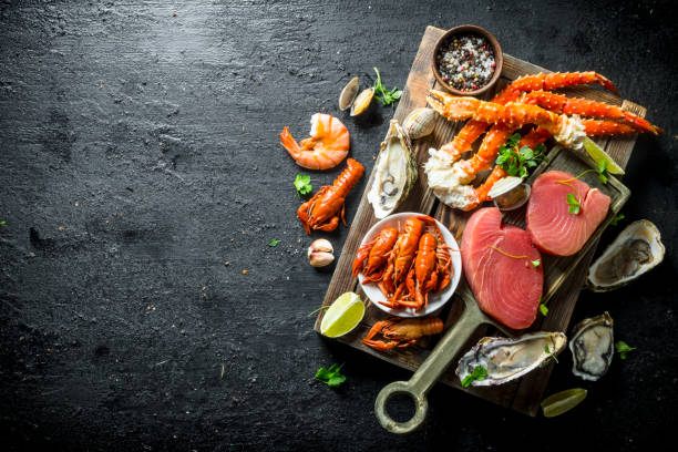 Raw tuna steak and seafood on wooden tray. Raw tuna steak and seafood on wooden tray. On black rustic background crustacean stock pictures, royalty-free photos & images