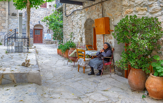 Senior greek woman sitting in front her house in Mesta which is a Greek traditional village on the island of Chios. Mesta has been added to the representative List of the Intangible Cultural Heritage of Humanity of UNESCO.