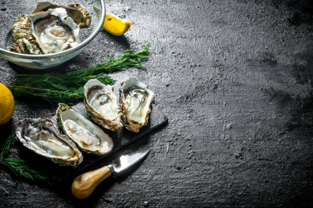 istock Fresh raw oysters on a stone Board and in a colander with lemon and dill. 1156019357
