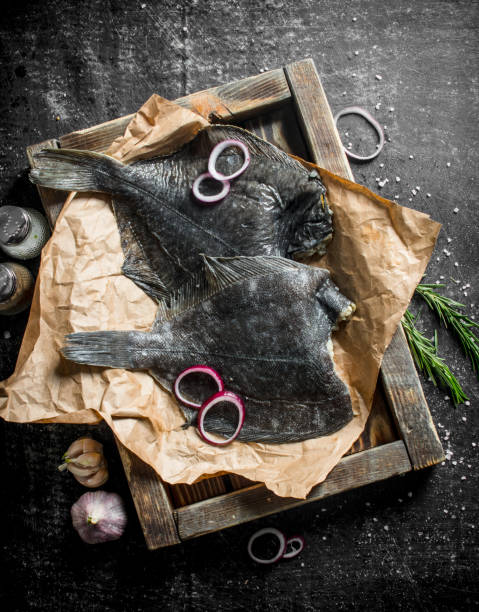 Raw fish on tray with garlic, chopped onion and rosemary. Raw fish on tray with garlic, chopped onion and rosemary. On dark rustic background turbot stock pictures, royalty-free photos & images
