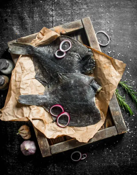 Raw fish on tray with garlic, chopped onion and rosemary. On dark rustic background