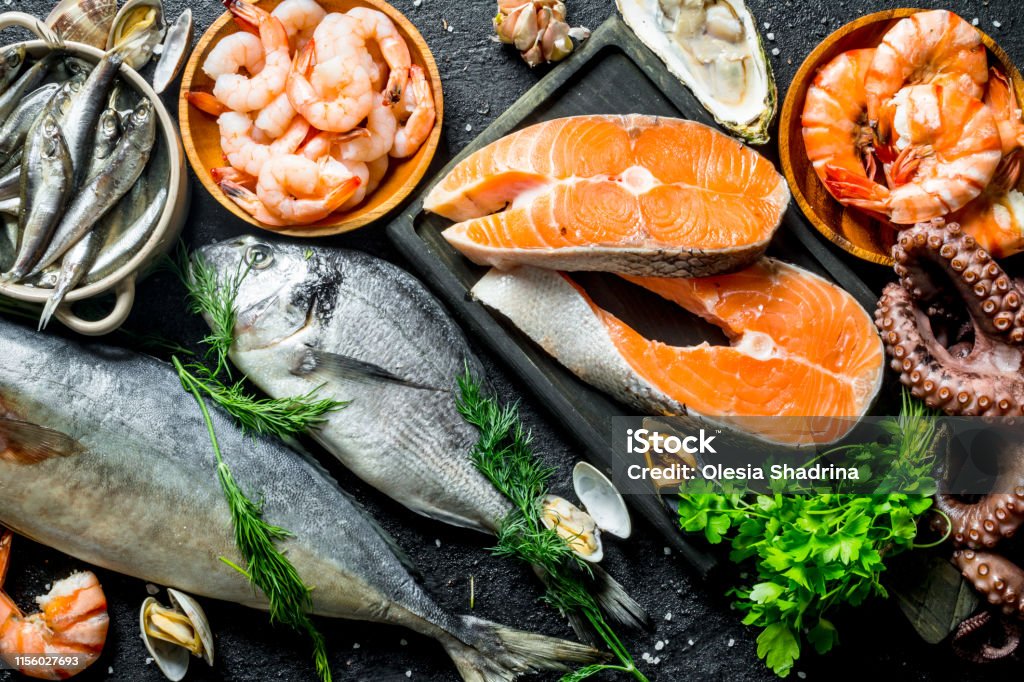 Fresh salmon steak with a variety of seafood and herbs. Fresh salmon steak with a variety of seafood and herbs. On black rustic background Fish Stock Photo