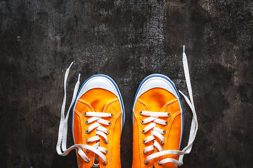 yellow-orange sneakers with untied laces on a dark concrete background. Copy space. View from above
