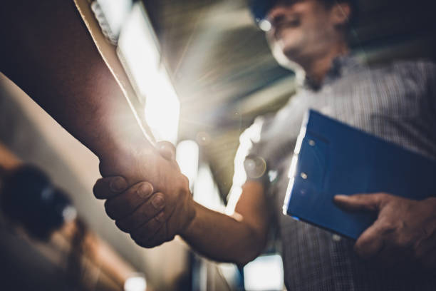 Close up of inspector shaking hands with unrecognizable person in a factory. Low angle view of manager greeting unrecognizable person in industrial building. working class stock pictures, royalty-free photos & images
