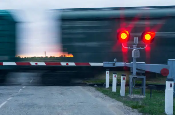Two traffic lights with red light and barrier in the background moving wagons and sunset