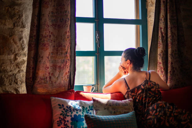 istock Mid aged woman is drinking coffee in front of the window 1156060904