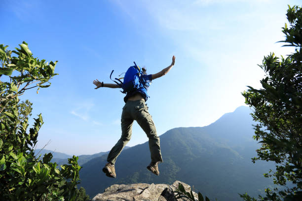 istock Successful young woman backpacker jumping on cliff's edge 1156061892