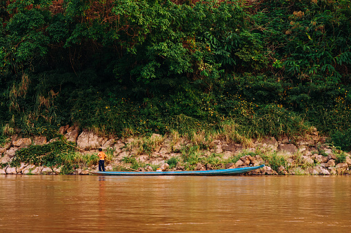 APR 3,2018 Luang Prabang, Laos - Asian local fisherman on blue wooden boat and rural scene of Mae khong river with lush green shoreline